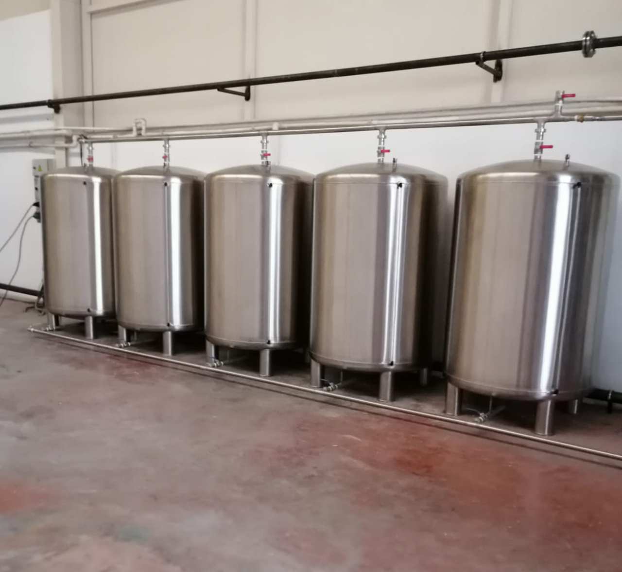 Row of vertical stainless steel storage tanks in a production room