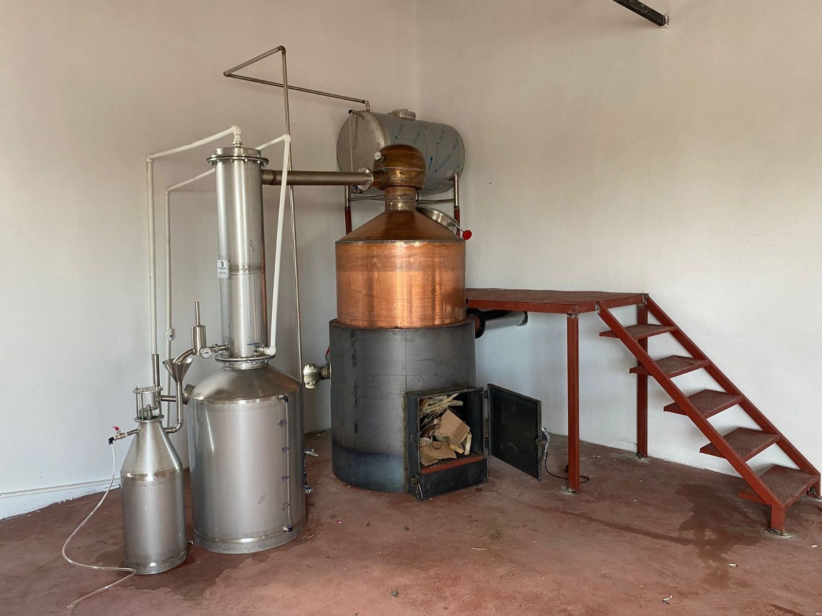 Solid-fuel copper distillation still with firebox and access stairs